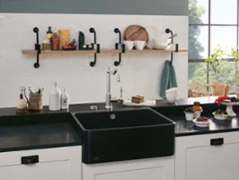 A black butler sink on a black worktop next to bowls and plates of fruit and muffins.