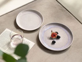 Perlemor Sand & Like Pearl – Natural Details, Timeless Beauty A close-up table view featuring Villeroy & Boch’s Perlemor Sand plates in soft beige tones and a Like Pearl water glass. One plate is styled with a halved fig, adding a subtle, natural accent to the elegant table arrangement. The scene highlights organic textures and calm, harmonious design.