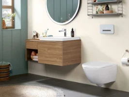 Modern bathroom with a round mirror above a wooden vanity unit, a floating toilet and a wall shelf with accessories and towels. On the left there is a window with sunlight.