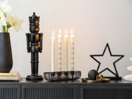 A dark vase, a black nutcracker A dark vase, a black nutcracker, four lit candles, star-shaped decorations and small ornaments arranged on a cupboard.
