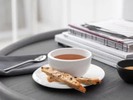Eine NewMoon Teetasse mit Untertasse mit Biscotti auf einem Tablett neben Büchern und einem Löffel.