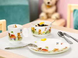 A Hungry as a Bear breakfast set with a bowl of muesli and fruit on a table, along with a cup, cutlery and a teddy bear in the background.
