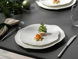 Un plato Pura blanco con pequeños aperitivos, incluyendo una torre de pepino, en una mesa puesta con decoración festiva.