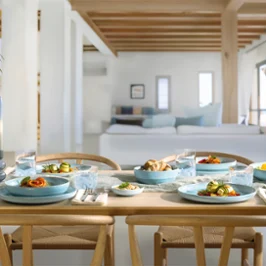 A wooden dining table for four people with blue Perlemor Aqua plates in a bright, modern living area.