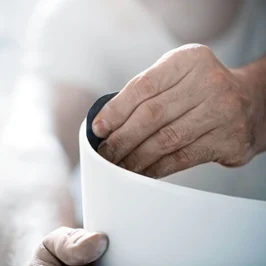 Une personne ponce le bord d’une surface blanche avec du papier de verre, gros plan sur les mains et l’objet traité.