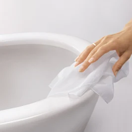 Une main portant une bague essuie des WC en céramique blanche avec un chiffon blanc.