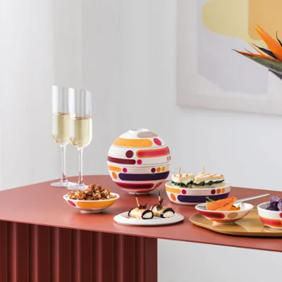 La Boule Miami with Manufacture Blanc Collier Vase in modern arrangement A modern table setting with La Boule Miami, assorted snacks, two champagne glasses, and a white Manufacture vase Collier with orange flowers.