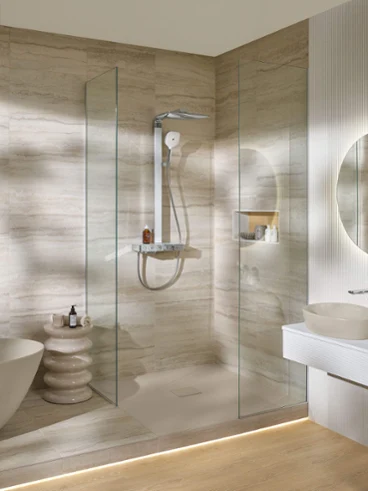 Salle de bains moderne avec douche vitrée, lavabo mural, miroir rond et serviettes empilées au sol.