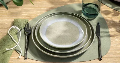 Vue du dessus d’un couvert de table avec des assiettes vert doux Perlemor Alga de Villeroy & Boch, superposées en nuances, combinées à un verre à eau Like Sage. Le service reflète une esthétique naturelle, calme et terreuse avec un caractère artisanal et de subtiles variations de tons.