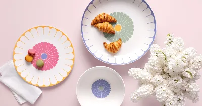 Three Villeroy & Boch Fleur plates with croissants and macarons next to white flowers on a light pink background.