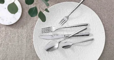 Elegant table decoration with modern Piemont cutlery and decorative greenery on a neutral tablecloth.