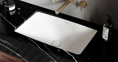 Lavabo moderno con piano in marmo nero, rubinetto dorato e maniglie abbinate. Sul ripiano ci sono un dispenser di sapone rotondo e una candela.