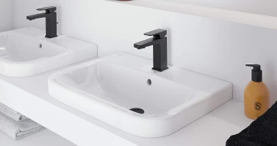 Bagno moderno con due lavabi bianchi e rubinetti neri su una mensola. Sulla mensola si trovano un dispenser di sapone e uno specchio. Gli asciugamani neri sono disposti ordinatamente su un ripiano inferiore.