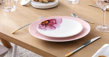 A minimalist dining table with elegant floral-patterned Rose Garden plates, complemented by modern, gold Ella cutlery.