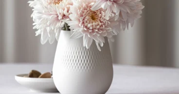 Vase Manufacture blanc avec chrysanthèmes rose pâle sur une table Vase Manufacture blanc avec des chrysanthèmes rose pâle sur une table, à côté d'une petite coupe avec des pierres.
