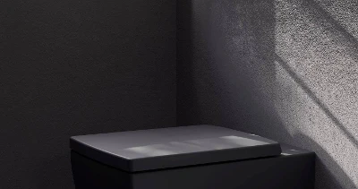 Bañera en un baño de estilo boho Cuarto de baño boho con bañera blanca Collaro y grifo mezclador Antao sobre suelo empedrado. Al fondo se ve un muro verde y una planta.