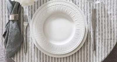 Elegant table decoration with white, embossed Cellini plate, flatware and folded gray napkin.