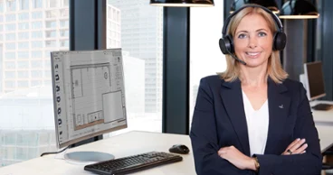 An employee sits at her desk looking at the camera. In the background you can see bathroom planning on the screen
