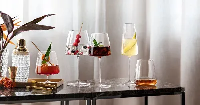 Various cocktails in elegant MetroChic glasses on a marble table next to a plant.
