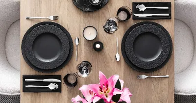 Modern table setting for two with black Manufacture crockery, Piemont cutlery and pink lilies as the centrepiece.