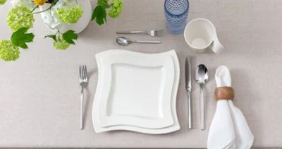 Modern top view of a single table setting featuring NewWave porcelain Klare, moderne Draufsicht auf ein einzelnes Gedeck mit NewWave Porzellantellern und Tasse, Boston Blue Longdrinkglas und passendem NewWave Besteck. Neutrale Töne und eine minimalistische Ästhetik vermitteln ein zeitgemäßes Ambiente.