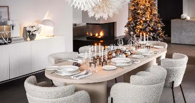 A modern dining room set for a meal with white Afina plates and candles. There are also two large paper stars as decorations, a decorated Christmas tree and a built-in fireplace.