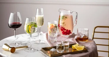 Glasses and jugs from the Villeroy & Boch Rose Garden collection on a round marble table with drinks and citrus fruits.