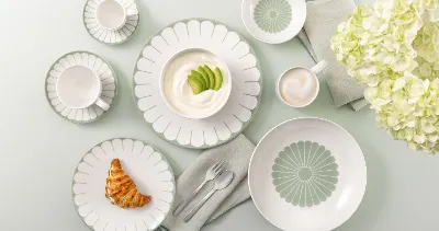 Table setting with Villeroy & Boch Fleur Vert plates, croissant, yogurt, coffee, and white flowers on a light green background.