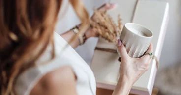 Eine Person hält eine Perlemor Duftkerze in der linken Hand und ein verpacktes Geschenk, geschmückt mit getrockneten Pflanzen.