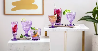 Villeroy & Boch purple Boston glasses filled with drinks on two white tables with gold legs