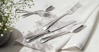 Villeroy & Boch Leandra cutlery on a white table with a white napkin next to flowers. 