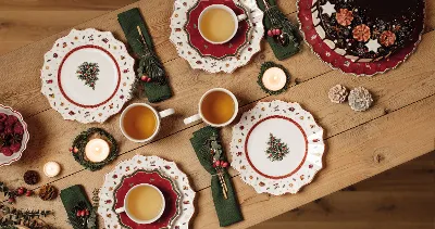 Festive table setting with Toy's Delight plates, cups of tea, a chocolate cake and candles on a wooden table.