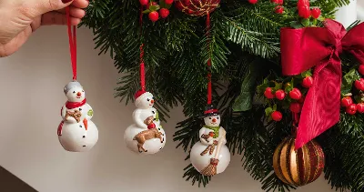 Snowman ornaments are hung by hand on a decorated Christmas tree with red ribbons, berries and baubles.