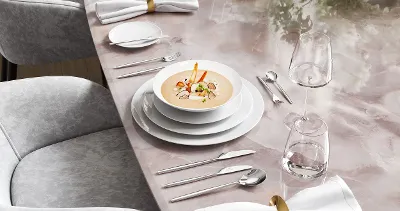 Elegant dining table with soup in white MetroChic plates, glasses and cutlery on a marble table, accompanied by flowers