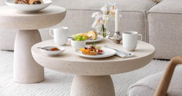 Un petit-déjeuner avec du café, de la confiture et des petits pains garnis sur une table basse beige avec de la vaisselle Afina blanche de Villeroy & Boch.