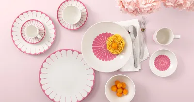 Table setting with Villeroy & Boch Fleur Cassis plates, pasta, clementines, and flowers on a pink background.