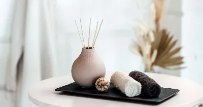 Beige Manufacture vase with fragrance sticks on a tray with towels.