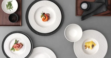 A formal table setting with a white and black plates, with food on it on a grey table.