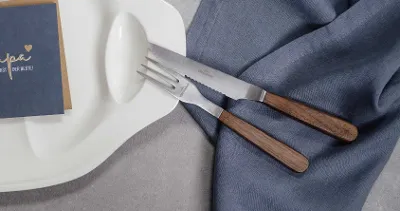 Elegant table decoration with modern wooden-handled Texas cutlery and a menu card on a textured linen napkin.