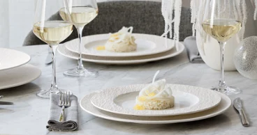 Elegant table setting with two Manufacture plates Elegant table setting with two Manufacture plates of dessert, wine glasses, and white decor on a marble surface.