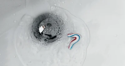 Zabrudzona umywalka z płynącą wodą Niewielka ilość pasty do zębów i wody spływa do odpływu umywalki w łazience, powodując powstawanie pęcherzyków wokół pokrywy odpływu.