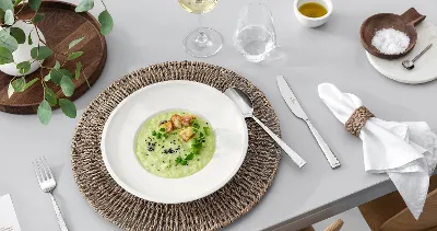 A dining table with Blacksmith cutlery, an Artesano plate filled with soup, a glass of white wine and rustic table decoration.