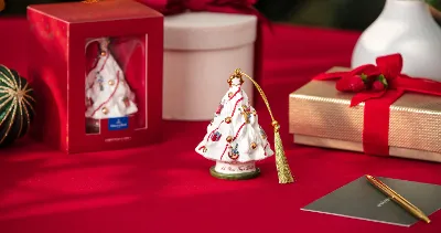 Decorazioni per l'albero di Natale in porcellana su un tavolo rosso, vicino a una confezione regalo, un imballaggio e una penna con decorazioni natalizie.