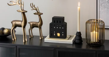 Two metal reindeer, candle holders Two metal reindeer, candle holders and a black, house-shaped lantern on a black sideboard.