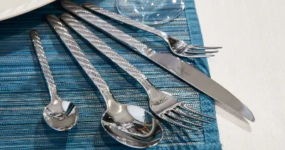 Silver Montauk flatware set arranged on a blue woven placemat next to a white plate and a glass.