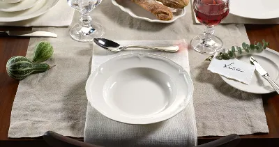 Dining table with Manoir plates with bread and decorative pumpkins on a rustic wooden table.