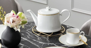 Elegant teapot by Chateau Septfontaines next to a stone vase by Manufacture on a stylish marble table presenting a refined decor