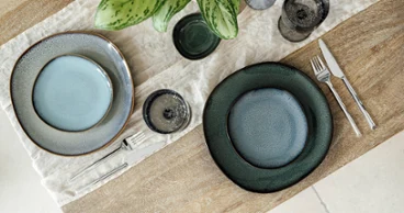 Vista dall’alto di piatti in gres Villeroy & Boch Lave in diversi colori, con due set blu su un tavolo in legno.