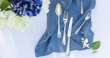 Eleganti decorazioni per la tavola con le posate Mademoiselle su un tovagliolo di lino blu e un bouquet di fiori.