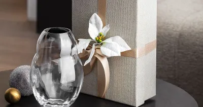 A table with a wrapped gift box, adorned with a white bow and a decorative Rose Garden Home glass vase